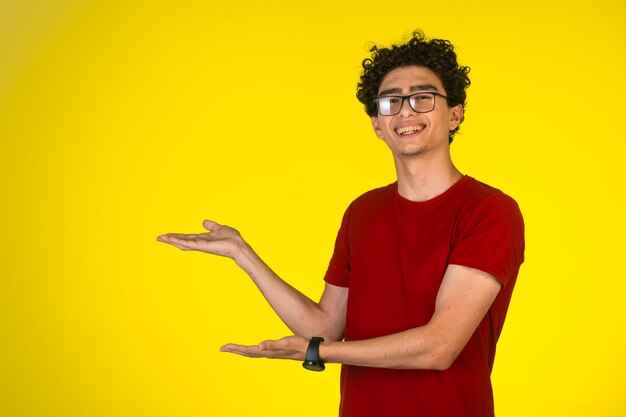 Homme en chemise rouge faisant la présentation avec des gestes de main avec joie et s'amuser.