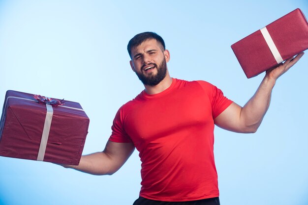 Homme en chemise rouge tenant des coffrets cadeaux à deux mains.