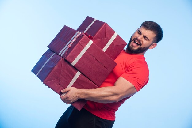 Homme en chemise rouge tenant un stock lourd de coffrets cadeaux.