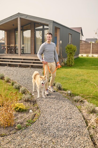 Homme avec chien en laisse marchant près de la maison de campagne