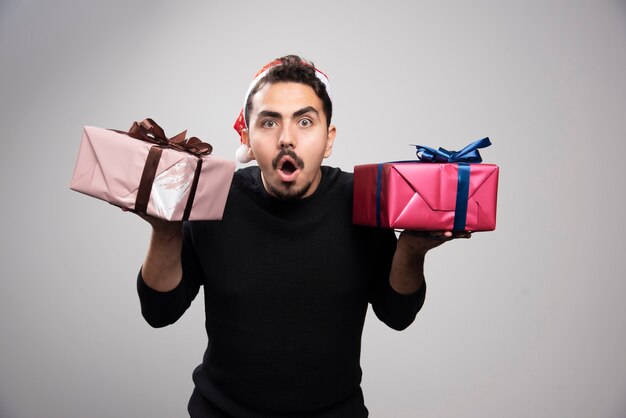 Photo gratuite un homme choqué dans un chapeau de père noël tenant des cadeaux du nouvel an.