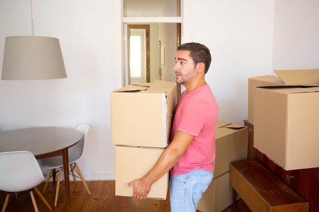 Homme ciblé transportant des boîtes en carton dans un nouvel appartement, emménageant dans un nouvel appartement
