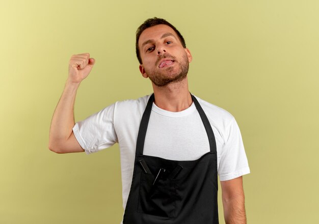 Homme de coiffeur en tablier à la recherche de l'avant poing serrant, concept gagnant debout sur mur léger