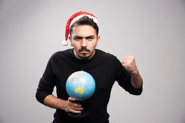 Homme en colère au chapeau du père Noël montrant un poing et tenant un globe.
