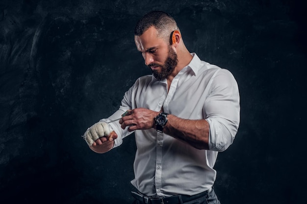 Photo gratuite un homme en colère brutal en chemise blanche porte une protection sur son poing avant de se battre dans un studio sombre.