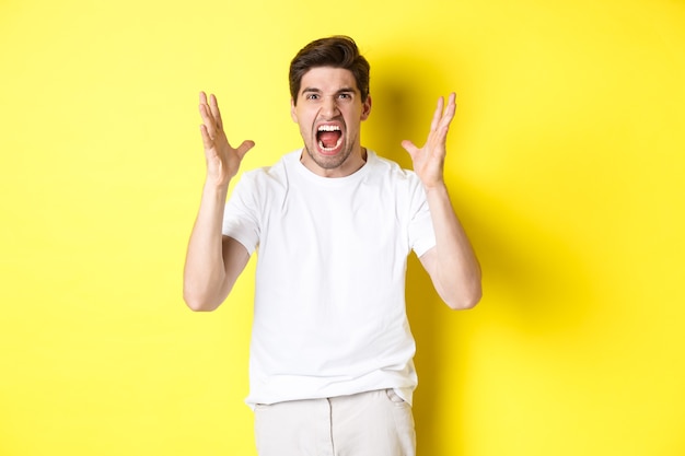 Homme en colère criant et serrant la main, grimaçant de haine, debout haineux sur fond jaune. Copier l'espace