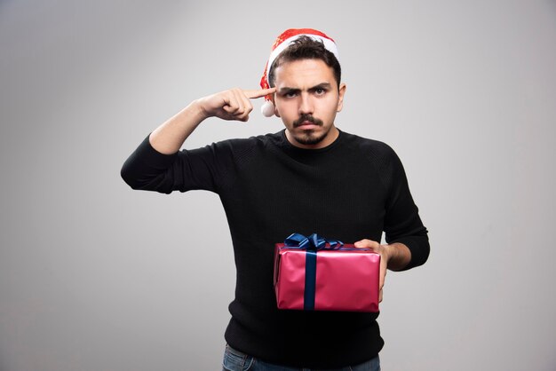 Homme en colère tenant une boîte-cadeau sur un mur gris.