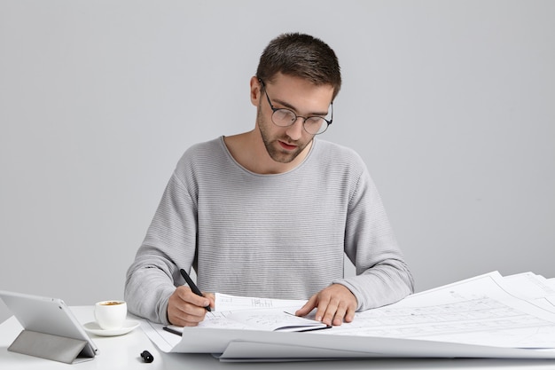 Homme concentré sérieux dessine des croquis, prépare un plan, utilise une tablette moderne