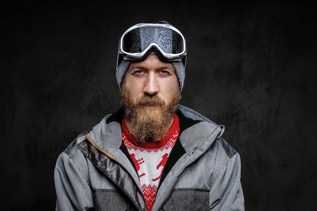 Homme confiant avec une barbe rouge portant un équipement complet pour le snowboard extrême, regardant une caméra avec un regard sérieux