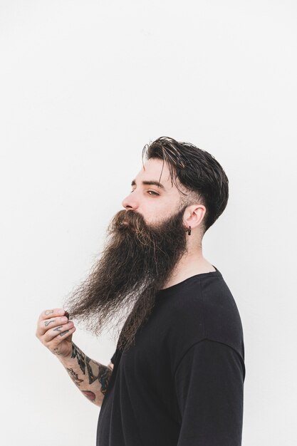 Homme confiant touchant sa barbe debout sur fond blanc