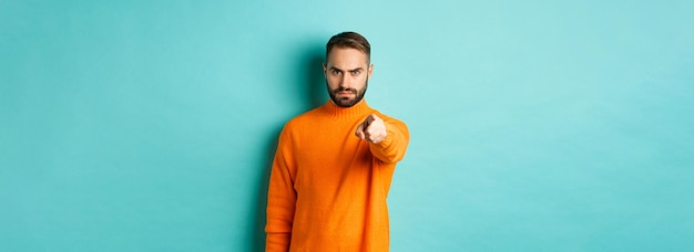 Photo gratuite un homme confiant vous blâme en fronçant les sourcils et en pointant le doigt sur la caméra