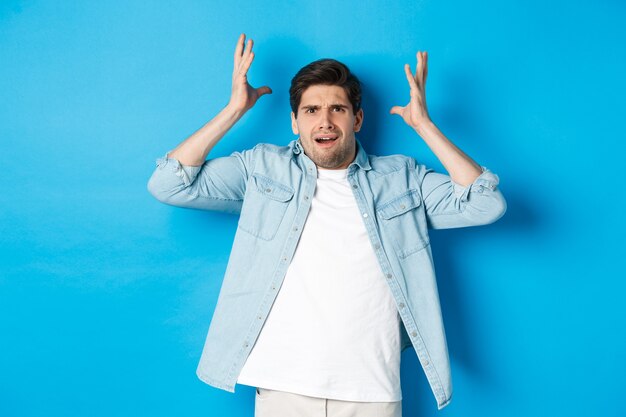 Homme confus et dérangé se tenant la main près de la tête, l'air frustré, debout bouleversé sur fond bleu