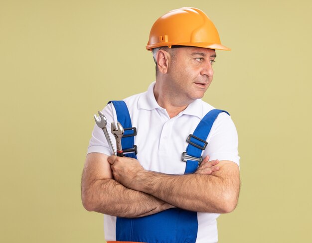 Homme de constructeur adulte confiant se tient avec les bras croisés à côté isolé sur mur vert olive