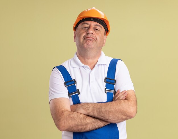 Homme de constructeur adulte confiant se tient avec les bras croisés sur vert olive