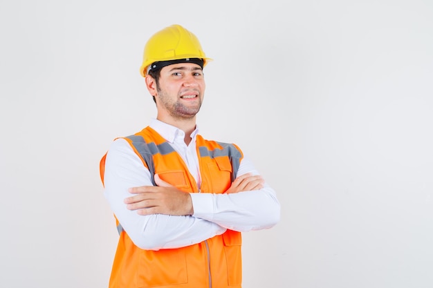 Homme de constructeur debout avec les bras croisés en chemise, uniforme et à la cerise. vue de face.