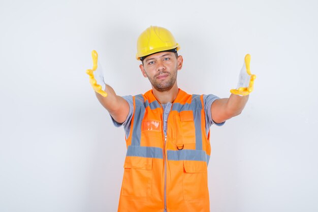 homme constructeur faisant passer le geste avec les mains en uniforme, casque, gants, vue de face