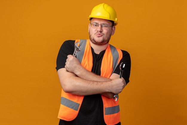 Homme de constructeur en gilet de construction et casque de sécurité tenant une clé regardant la caméra avec une expression confiante