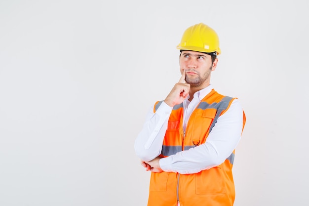 Homme de constructeur mettant le doigt près de la bouche en chemise, uniforme et pensif. vue de face.