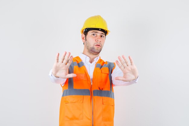 Homme de constructeur montrant assez de geste en chemise, uniforme et à la recherche de sérieux. vue de face.