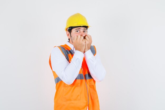 Homme de constructeur mordant les poings en chemise, uniforme et à la peur, vue de face.