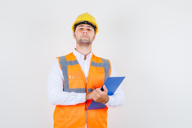 Homme de constructeur tenant le presse-papiers en chemise, uniforme et à la recherche stricte, vue de face.