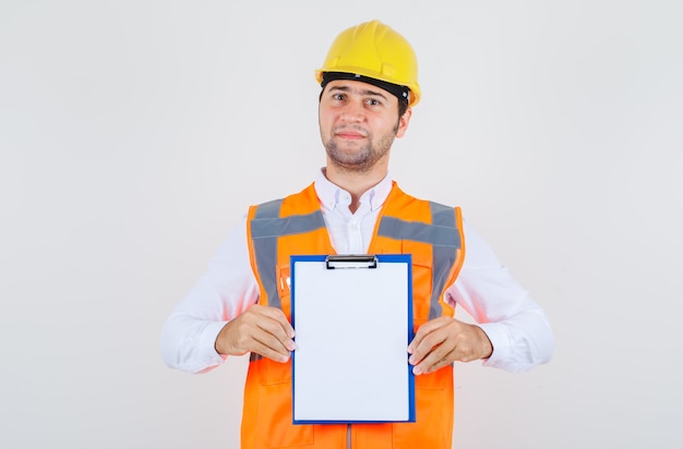 Homme de constructeur tenant le presse-papiers et souriant en chemise, uniforme, vue de face.