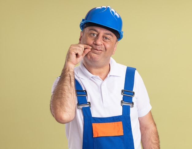 Homme de construction adulte caucasien en uniforme bouche zips isolé sur mur vert olive