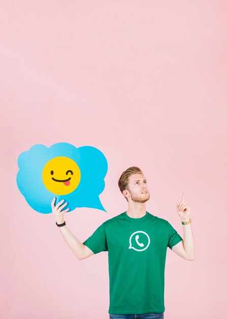 Homme contemplé pointant vers le haut tout en tenant la bulle de dialogue emoji clin d&#39;oeil