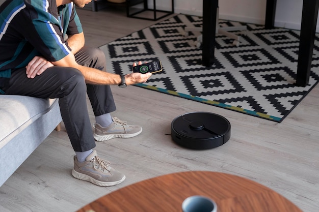 Photo gratuite homme contrôlant un robot aspirateur avec son téléphone