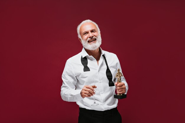 Un homme cool en chemise classique blanche tient un verre et une statuette de récompense