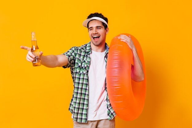 Un homme coquin de bonne humeur cligne de l'œil et pose avec une bouteille de bière et un cercle orange gonflable.