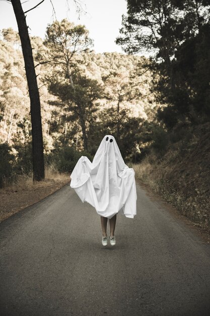 Homme en costume fantôme sautant sur une route de campagne