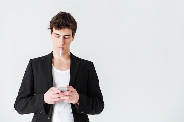 Homme en costume fumant une cigarette et utilisant un smartphone