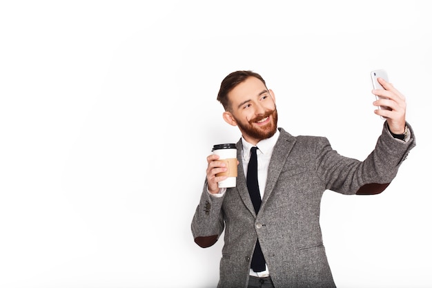 Homme en costume gris prend selfie avec du café dans son bras