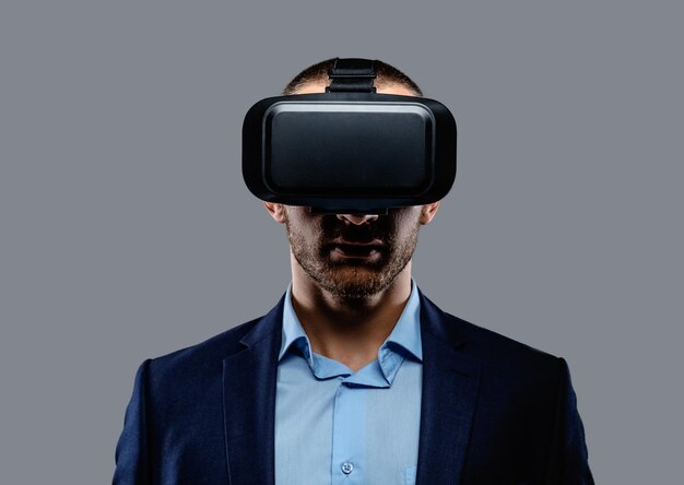 Homme en costume avec des lunettes de réalité virtuelle sur la tête. Isolé sur fond gris.