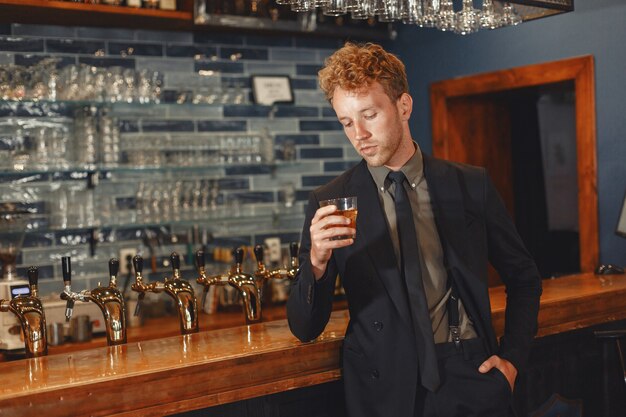 L'homme en costume noir boit de l'alcool. Un mec séduisant boit du whisky dans un verre.