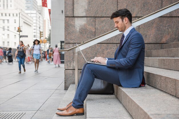 Homme en costume utilisant un ordinateur portable dans la rue