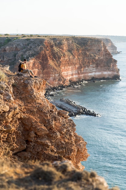 Photo gratuite homme sur le côté assis sur une côte et profiter de la vue