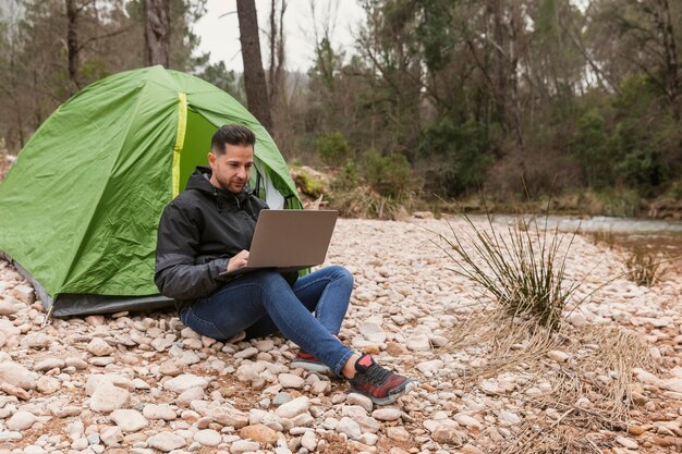 Homme à côté de la tente avec ordinateur portable