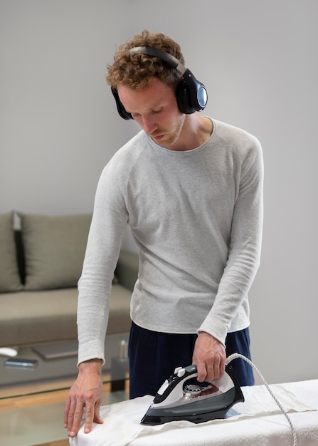 Photo gratuite homme de coup moyen avec une chemise de repassage d'écouteurs