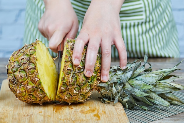 L'homme coupe un ananas frais sur une planche à découper en bois.