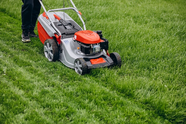 Un homme coupe de l'herbe avec une meuleuse à gazon dans la cour arrière.
