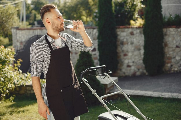 Photo gratuite homme coupe l'herbe avec tondeuse à gazon dans la cour arrière. mâle dans un tablier noir.