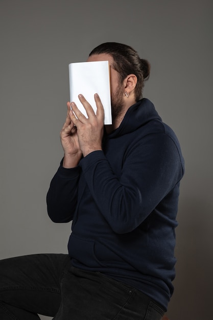 Homme couvrant le visage avec un livre en lisant sur un mur gris