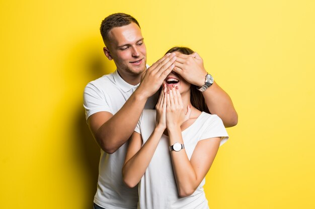 Homme couvrir les yeux sa petite amie surprise conceprt isolé sur jaune