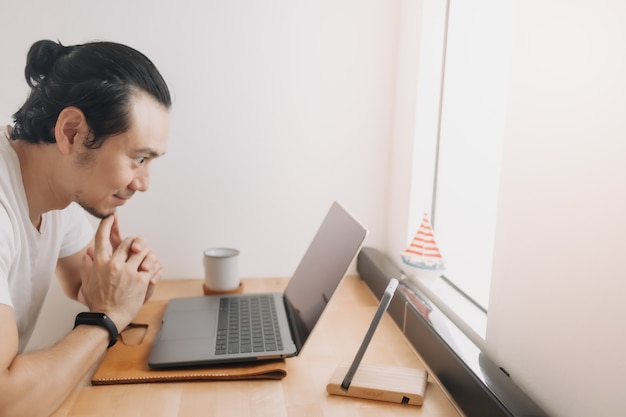 Un homme créatif travaille avec un ordinateur portable sur l'espace de travail du bureau en bois près des fenêtres