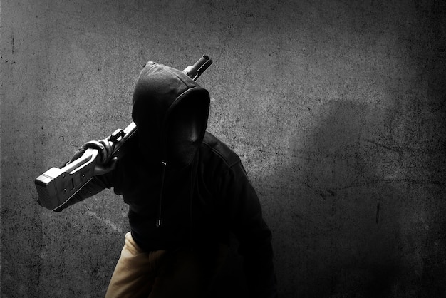 Homme criminel dans un masque caché tenant le fusil de chasse avec fond de mur noir