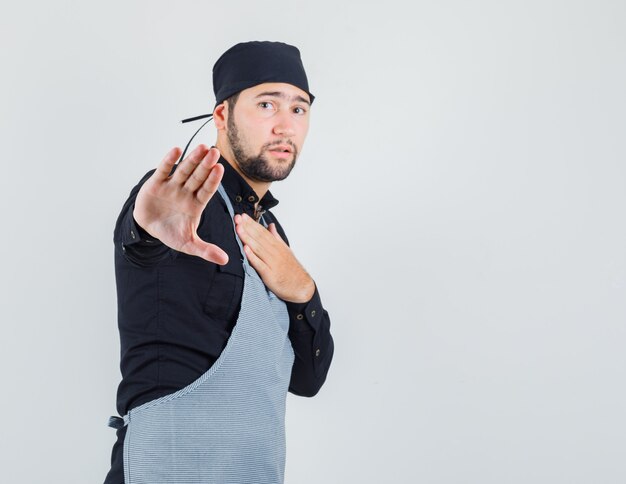 Homme cuisinier en chemise, tablier montrant le geste de refus et à la vue épuisée, vue de face.