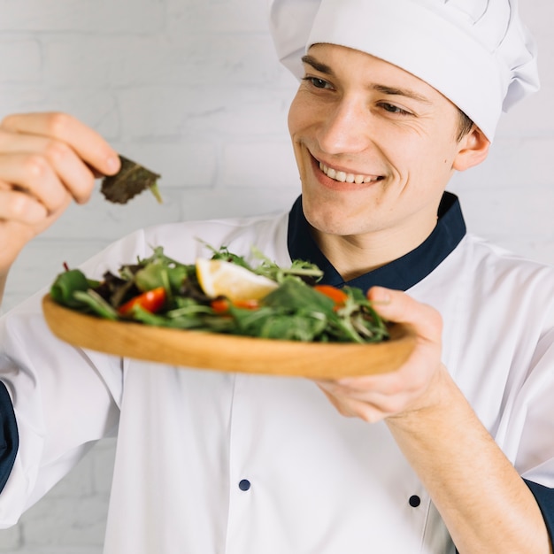 Photo gratuite homme cuisinier regardant une assiette en bois avec salade