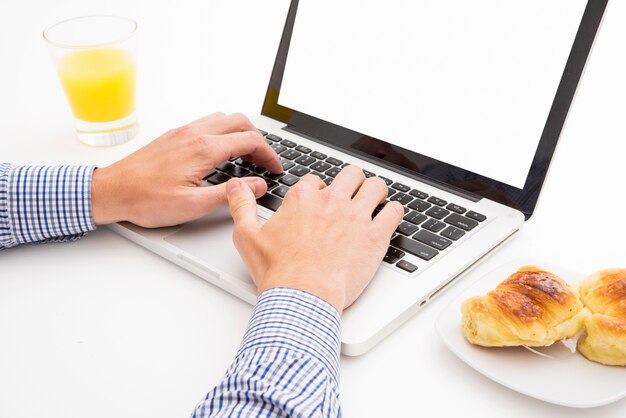 Homme dactylographie sur ordinateur portable avec petit-déjeuner sur la table blanche